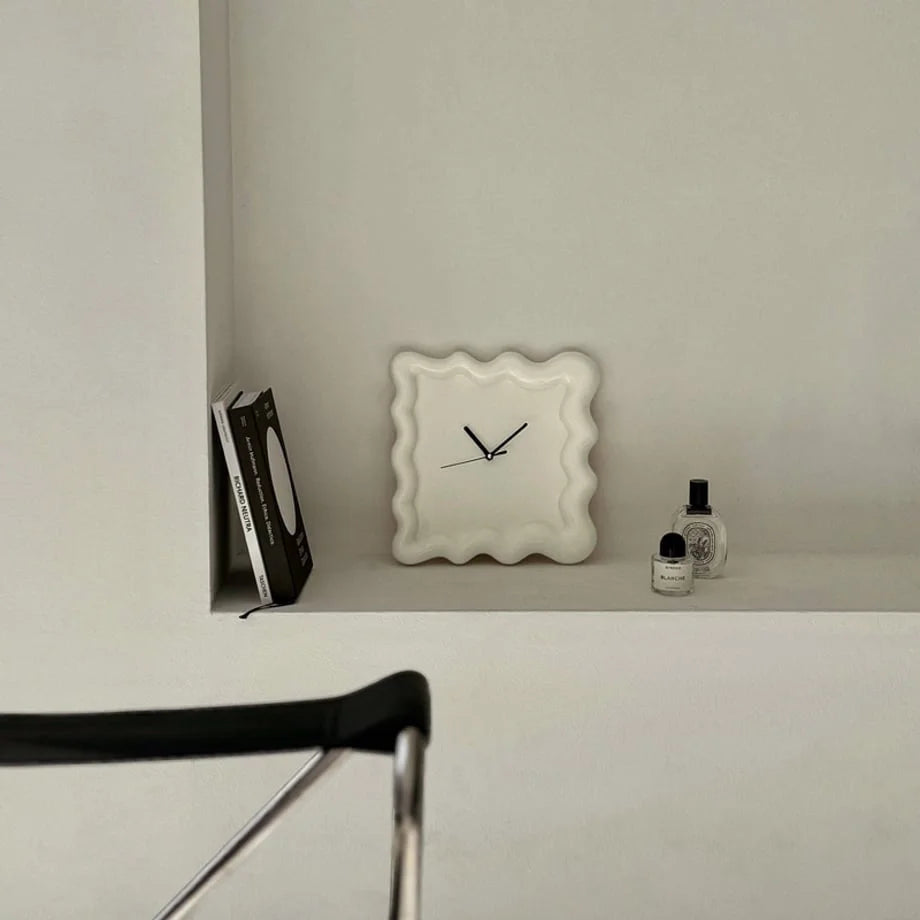 An off-white Wavy Squiggle Clock displayed on a built-in white shelf with books and perfume. - RoomDen