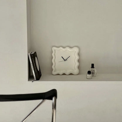 An off-white Wavy Squiggle Clock displayed on a built-in white shelf with books and perfume. - RoomDen