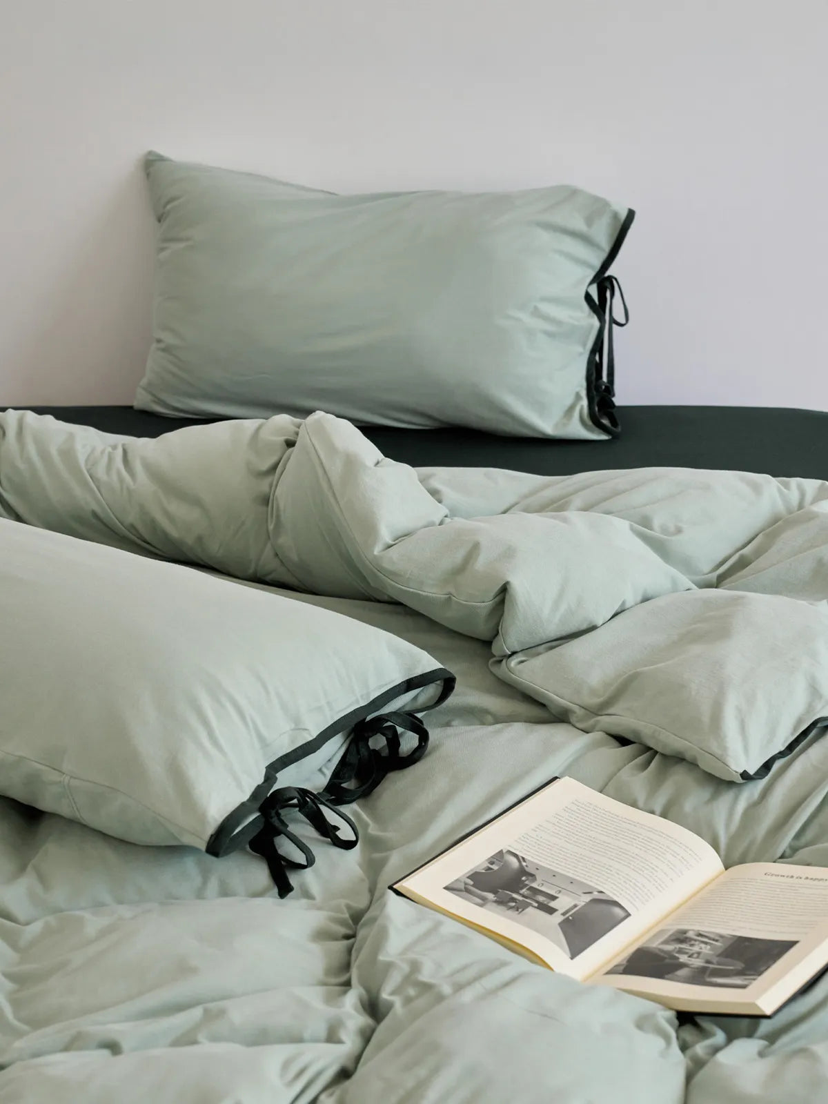 Soft Contrast Tie Washed Cotton Bedding Set in Sage Green & Black on a neatly made bed with a book. - RoomDen