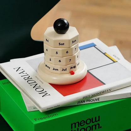 Close-up of the minimalist perpetual calendar on a stack of books, including "MONDRIAN". - RoomDen