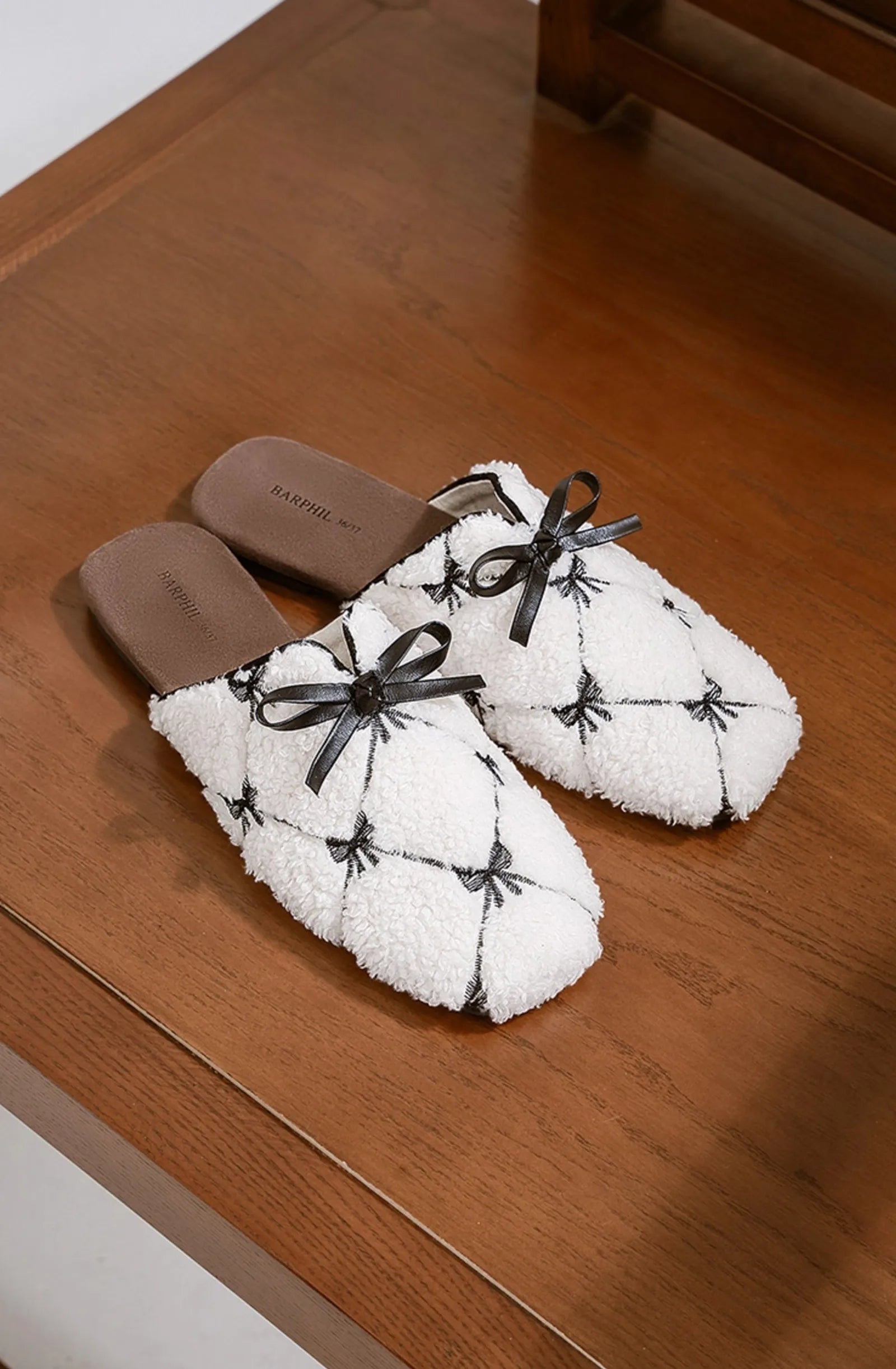 Soft white bedroom slippers with black stitching resting on wooden surface