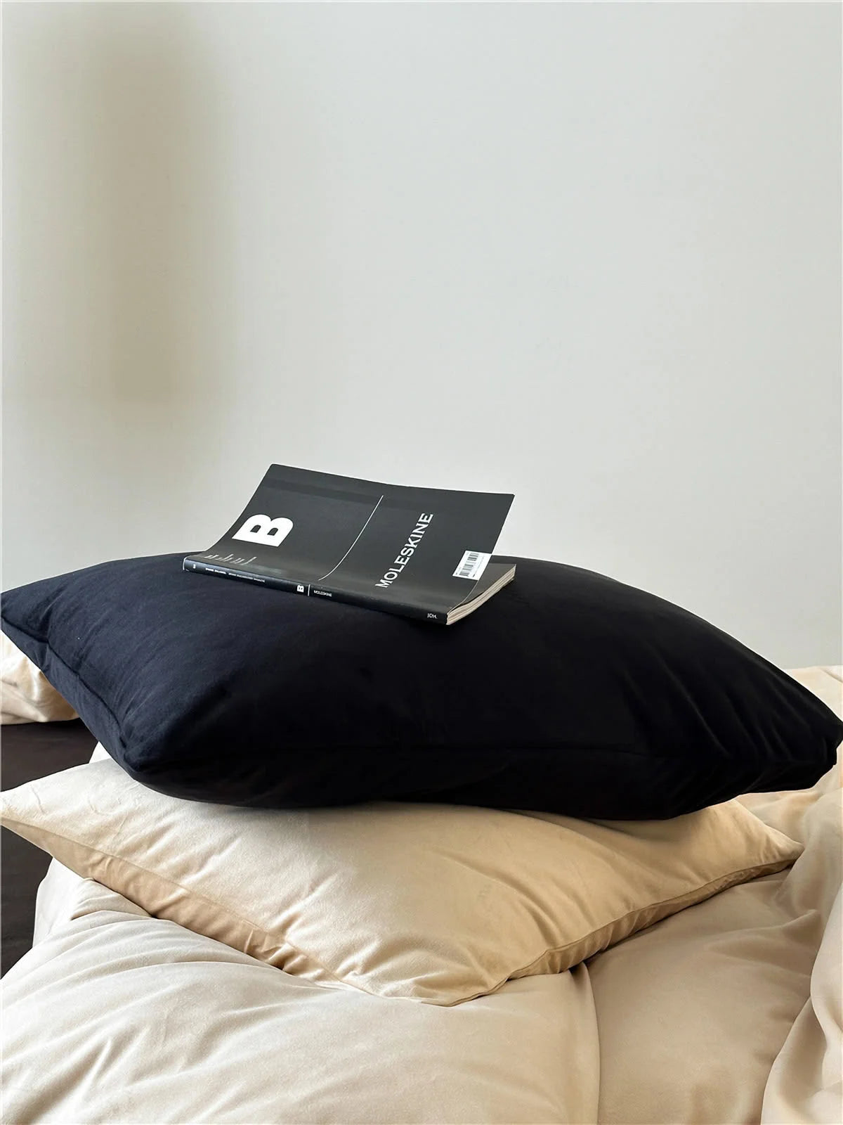 Close-up of a black velvet pillowcase showing its soft texture, stacked on a beige pillow. - RoomDen