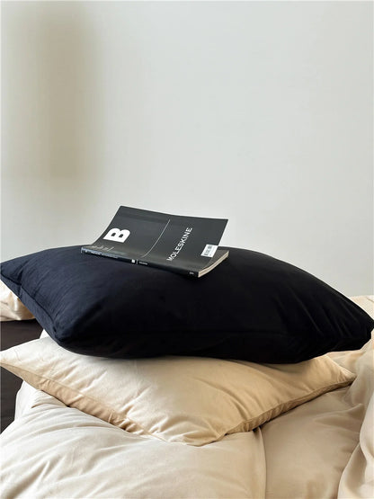 Close-up of a black velvet pillowcase showing its soft texture, stacked on a beige pillow. - RoomDen