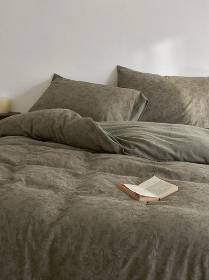 A cozy, rumpled bed with the earthy green botanical duvet cover and pillows, styled with an open book, creating a calm and inviting atmosphere.