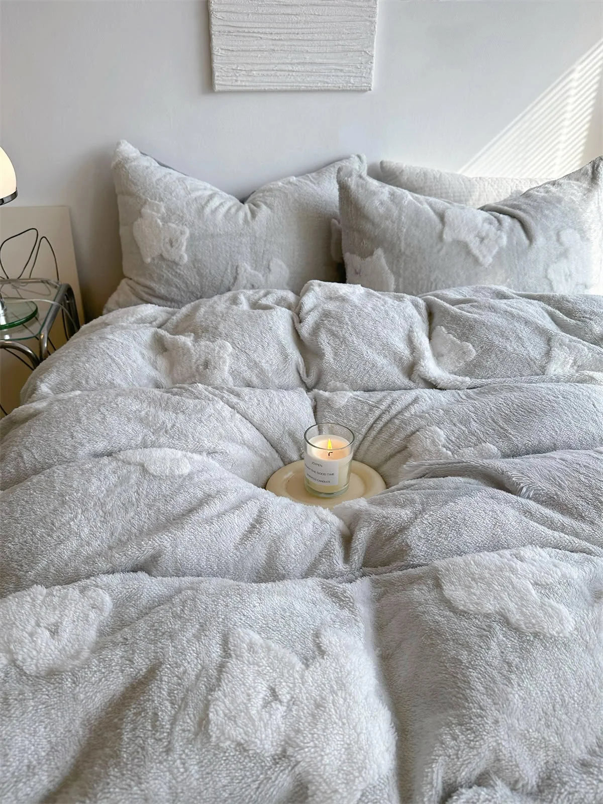 Close-up of the light grey flannel fleece bedding set variant, with a lit candle resting on the plush duvet. - RoomDen