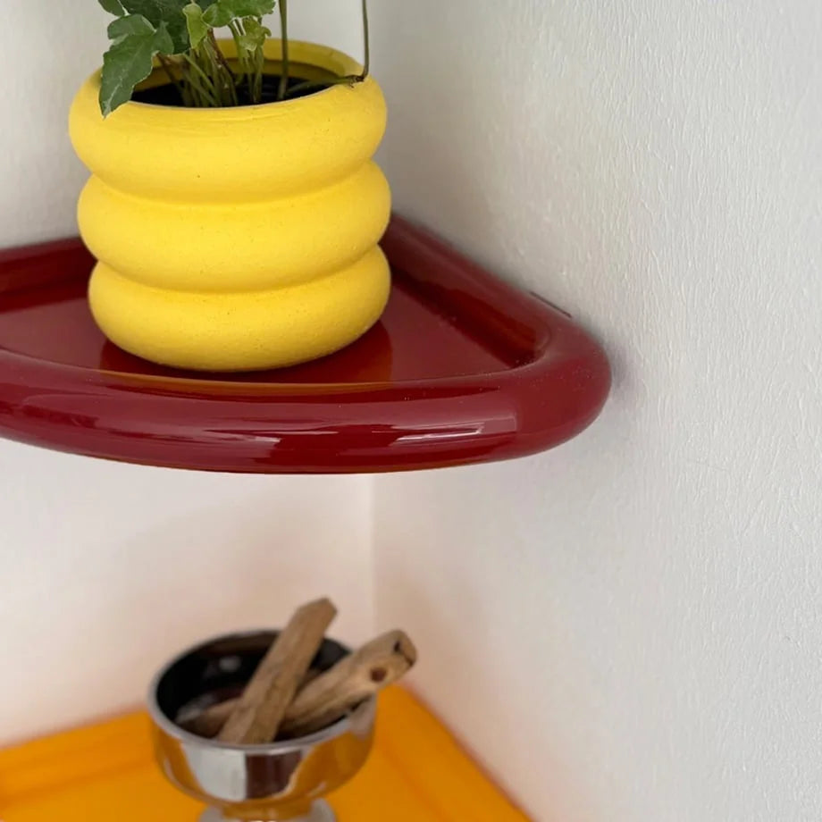 Detailed view of the glossy red finish on the Curved Corner Shelf, with a yellow shelf and decor below it. - RoomDen