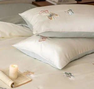 Close-up of two stacked pillows with delicate pink and blue butterfly embroidery - RoomDen