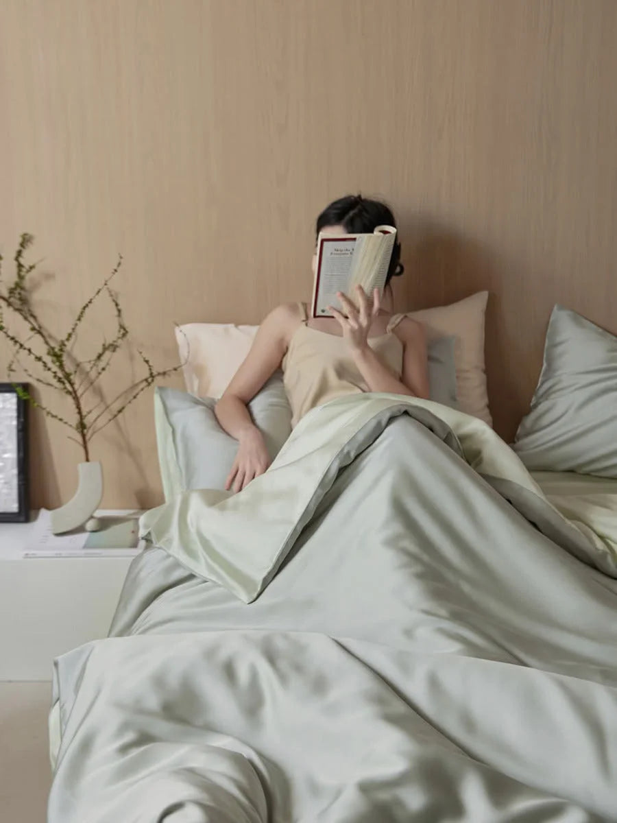 A person reading in bed, enveloped in the Sage Mist Cooling Tencel Bedding Set. - RoomDen