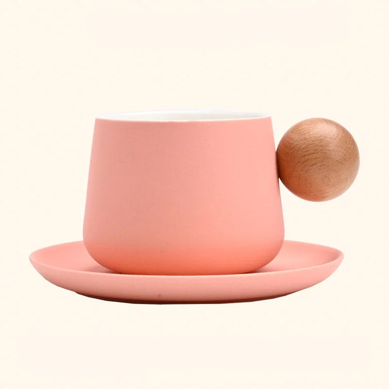 A studio shot of the Pink Frosted Ceramic Mug and Saucer Set with a wooden ball handle against a plain background. - RoomDen