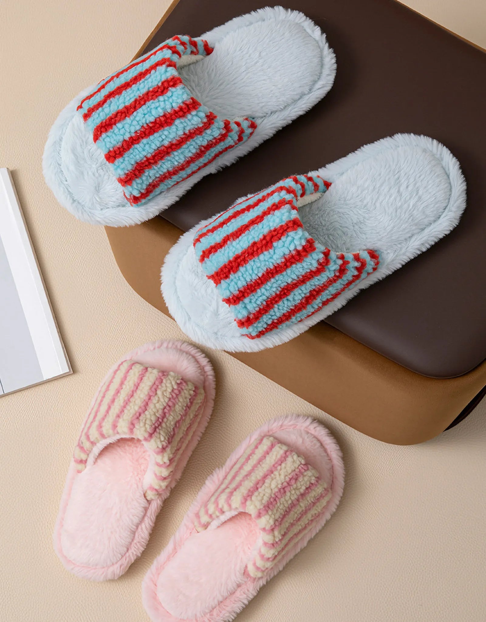 Blue and Red striped plush slippers next to Pink and Red striped slippers on a chair - RoomDen