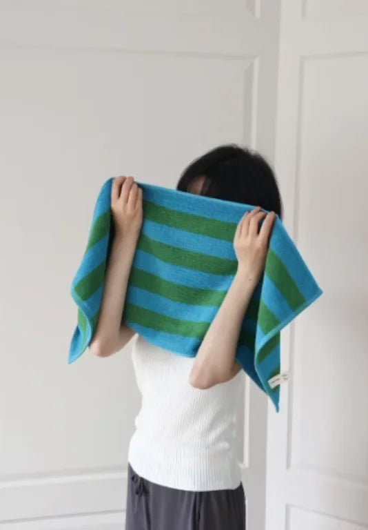 A person holding a blue and green striped cotton face towel in front of them in a bright, minimalist room. - RoomDen