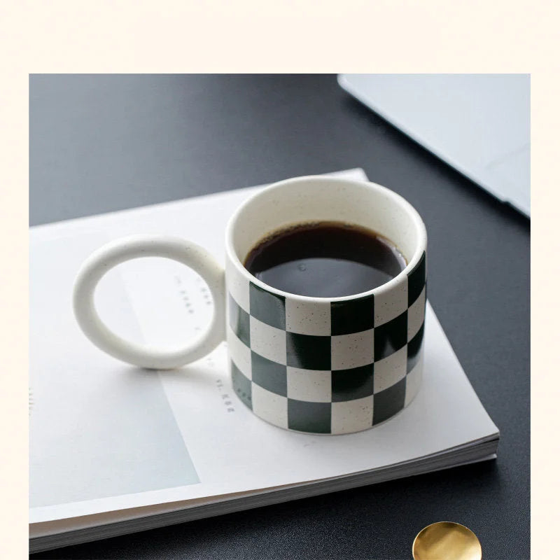 The Green Checkered Ceramic Mug with an Oversized Handle sitting on a magazine. - RoomDen