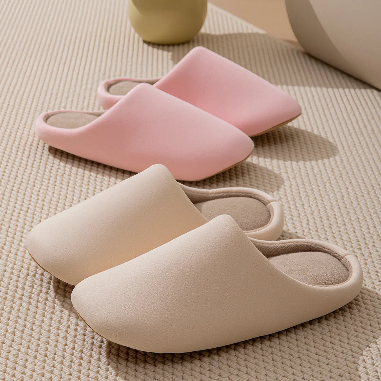 Pink and beige solid color slippers arranged on textured rug - RoomDen