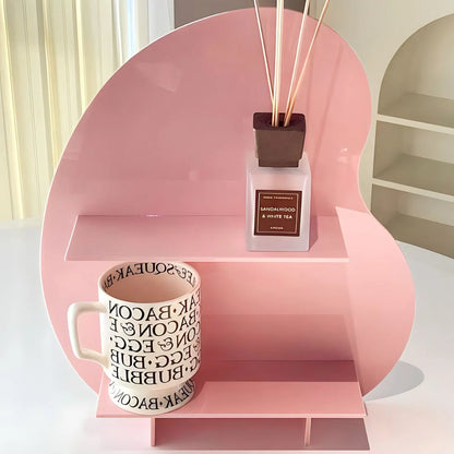 The pink wavy acrylic perfume stand holding a mug and a room diffuser, showing its vibrant color. - RoomDen