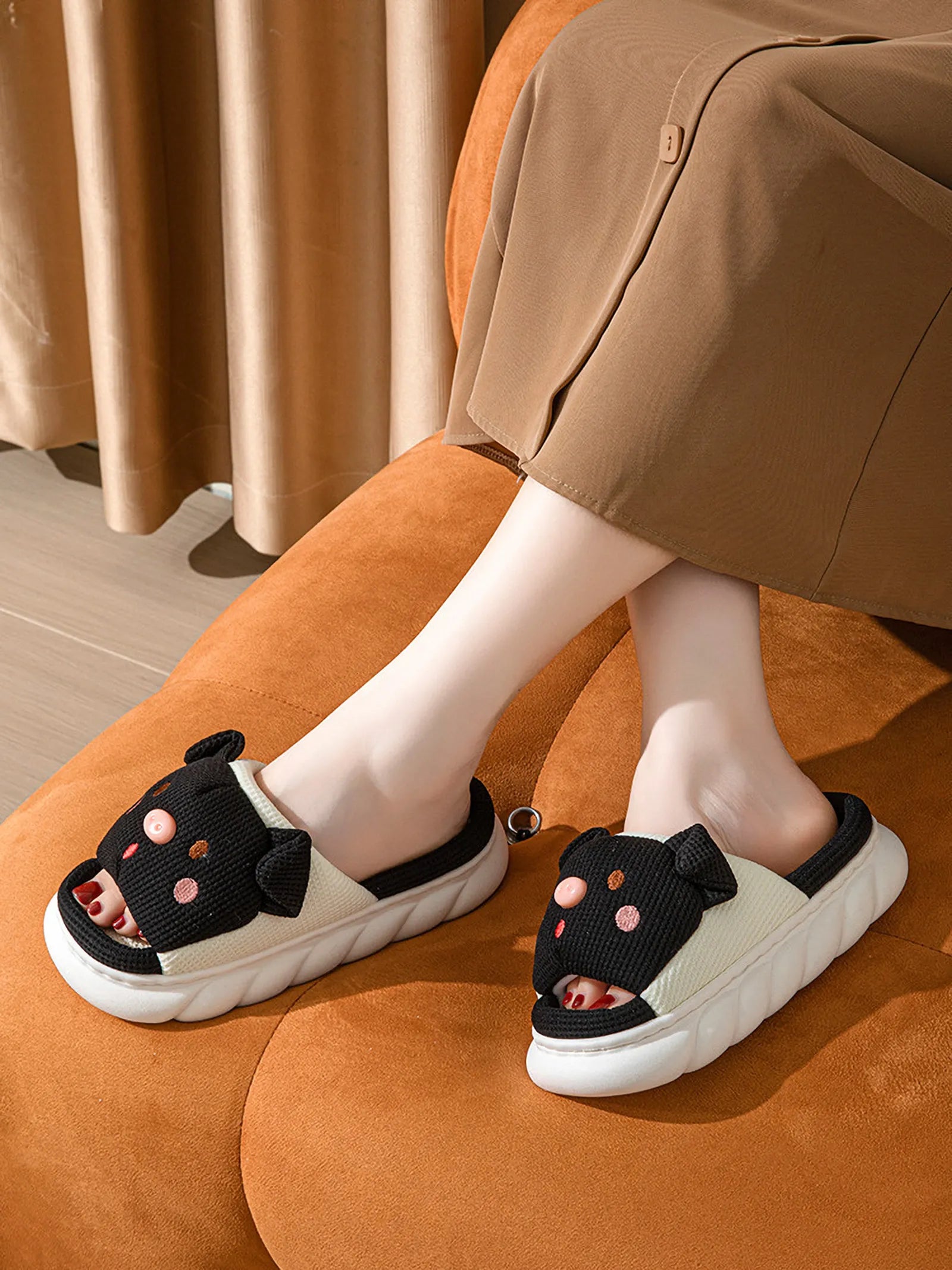 Woman wearing Black Waffle Textured Embroidered Pig Linen House Slippers sitting on an orange sofa - RoomDen