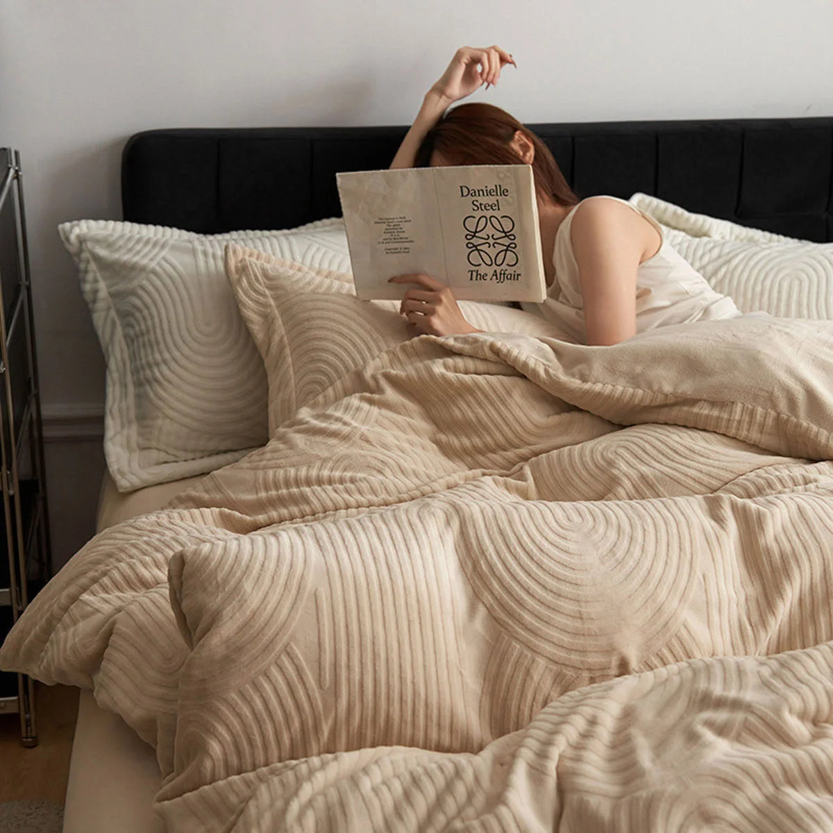 Woman reading a book while relaxing in the cozy Latte Beige Plush Wavy Arch Flannel Fleece Bedding Set. - RoomDen