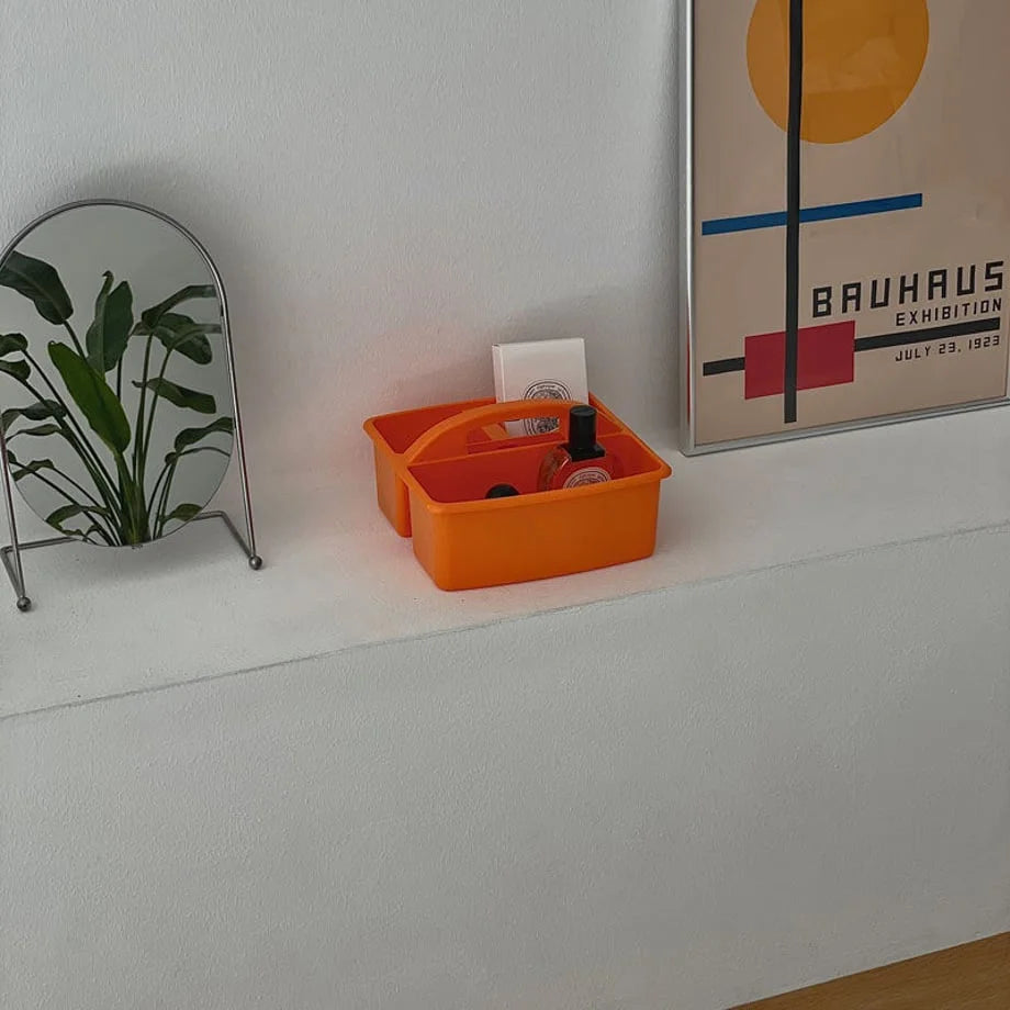 Orange organizer caddy holding beauty products on a white shelf, with a mirror reflecting a plant. - RoomDen