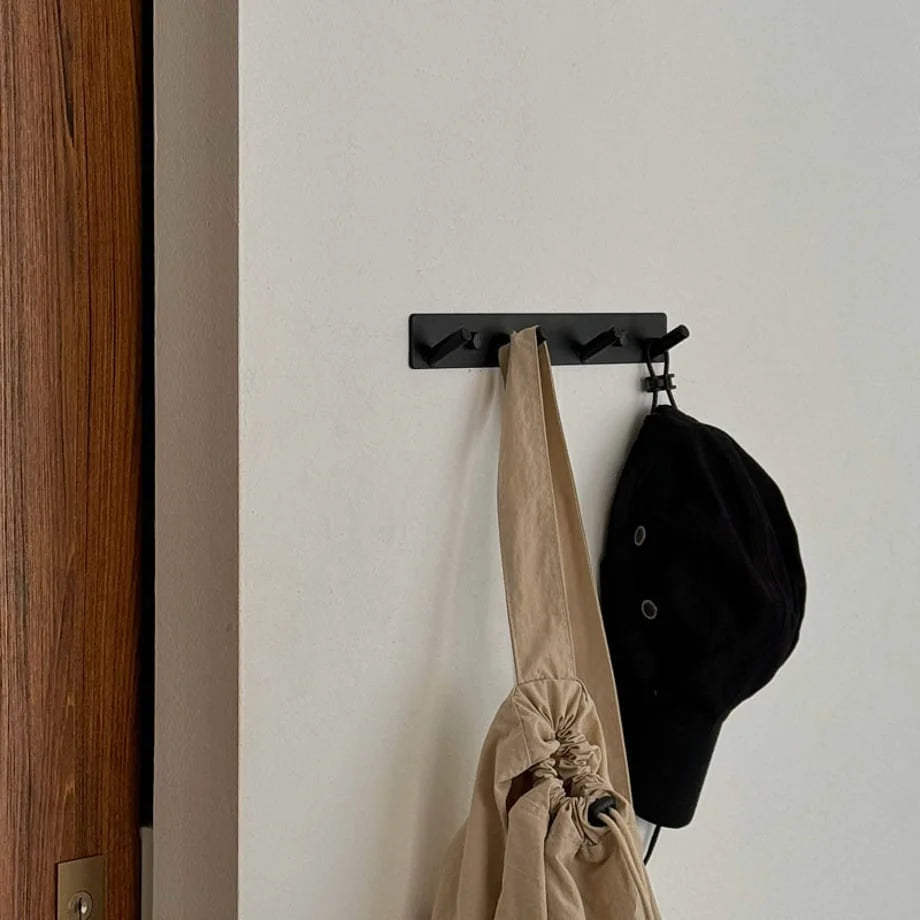 Black minimalist metal wall hooks holding a tote bag and a cap in a modern entryway - RoomDen.