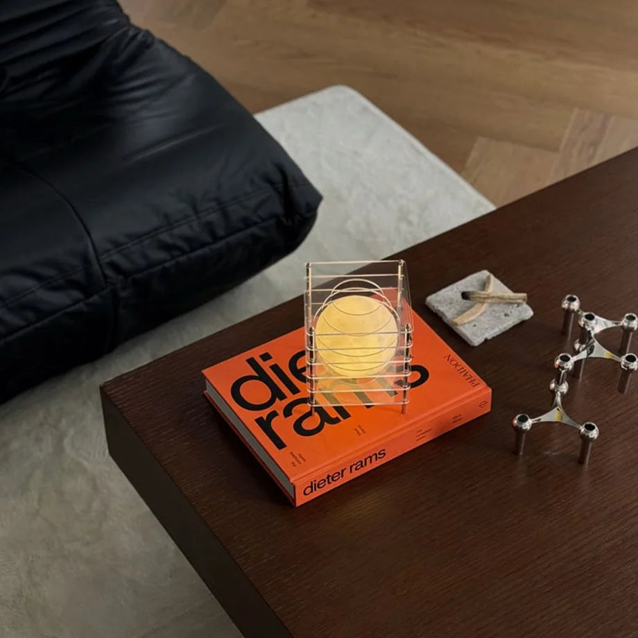 Crystal Clear Caged Moon Lamp displayed on a Dieter Rams art book on a dark wood coffee table - RoomDen