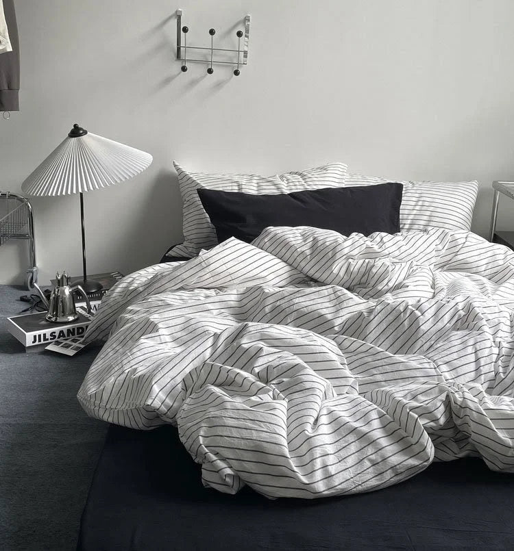 The pinstripe washed cotton duvet cover artfully rumpled on a bed with a black fitted sheet, creating a relaxed vibe. - RoomDen