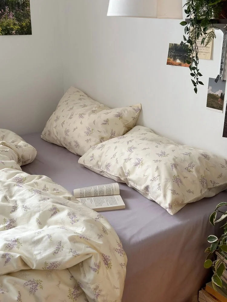 View of the wisteria floral pillowcases resting on a solid lavender fitted sheet - RoomDen.