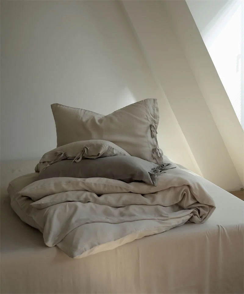 A neatly folded stack of the Oatmeal Beige Tencel duvet cover and pillows on a bed - RoomDen