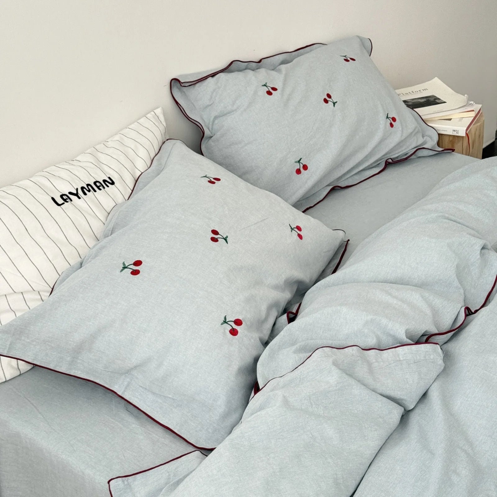 Detail shot of the dusty blue embroidered cherry pillowcases on a bed with a striped accent pillow.