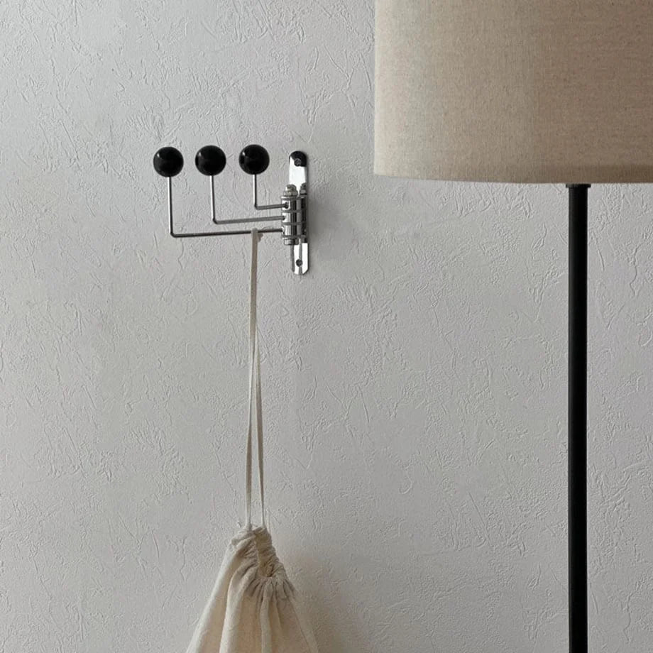 The black ball-end metal wall hook with its arms slightly pivoted, shown in a serene setting - RoomDen.