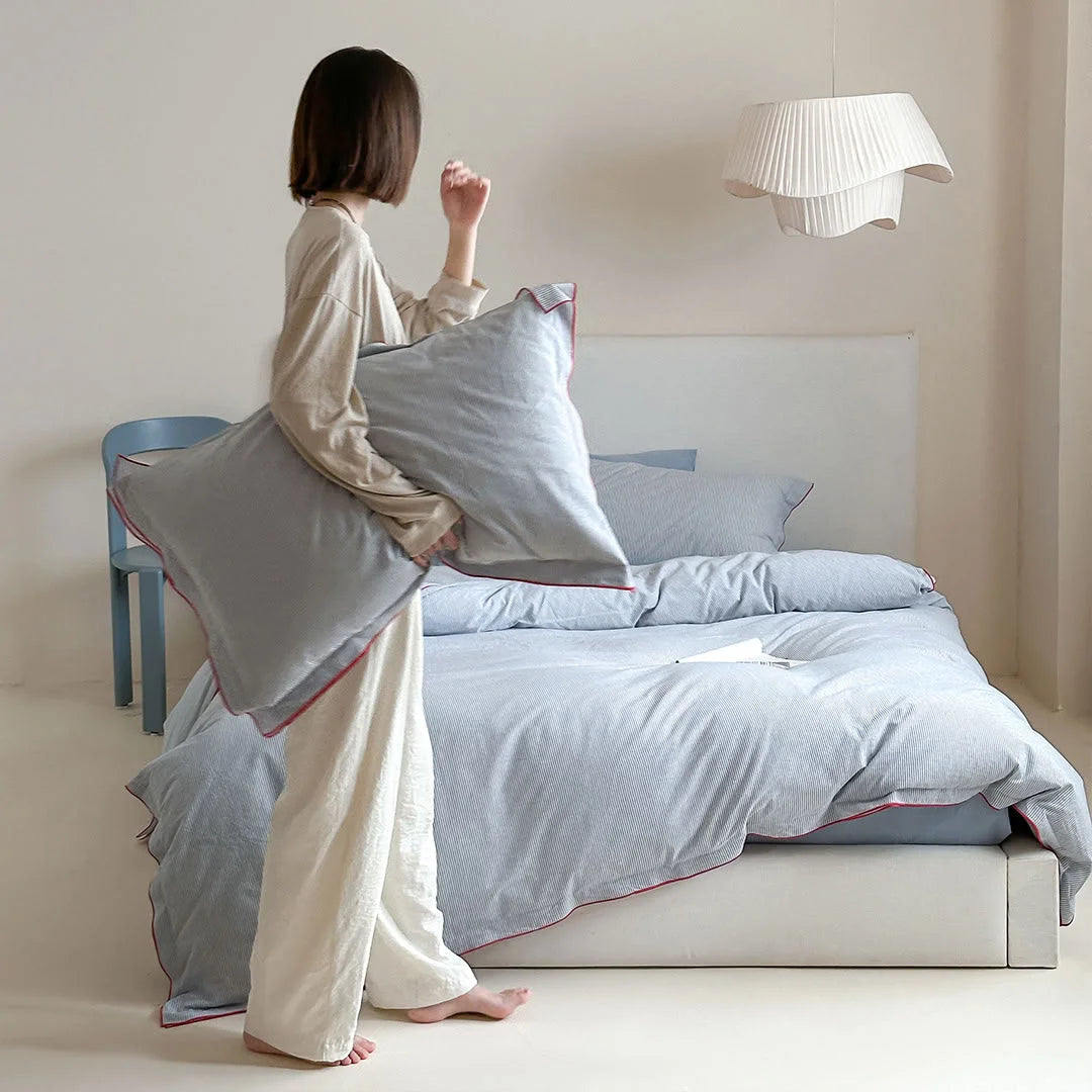 A woman holding a pillow from the Light Grey & Red Pinstripe Washed Cotton Bedding Set in a minimalist bedroom - RoomDen.