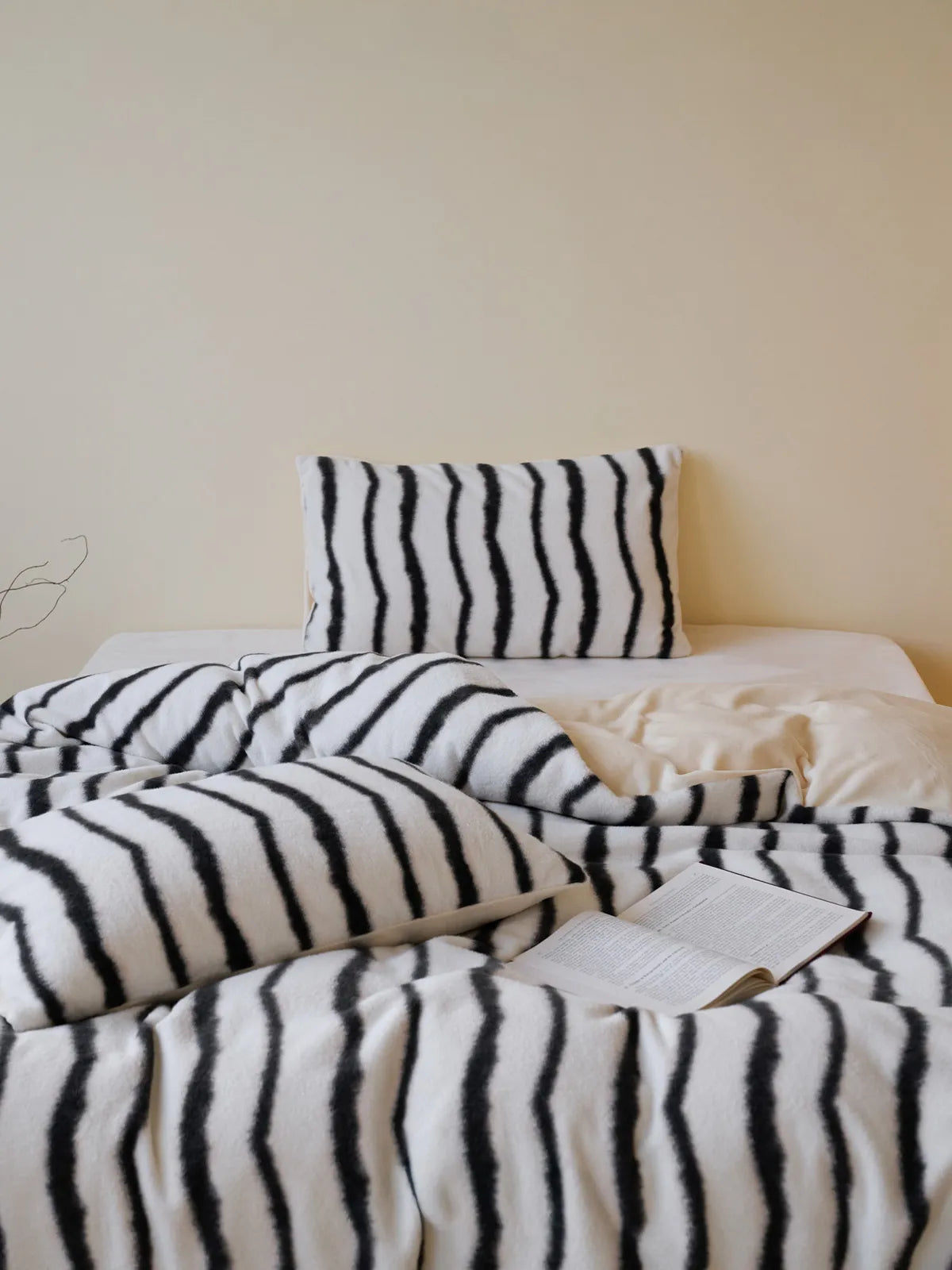 A cozy bed made with a black and white wavy striped flannel fleece duvet cover and pillows, with an open book on top - RoomDen.
