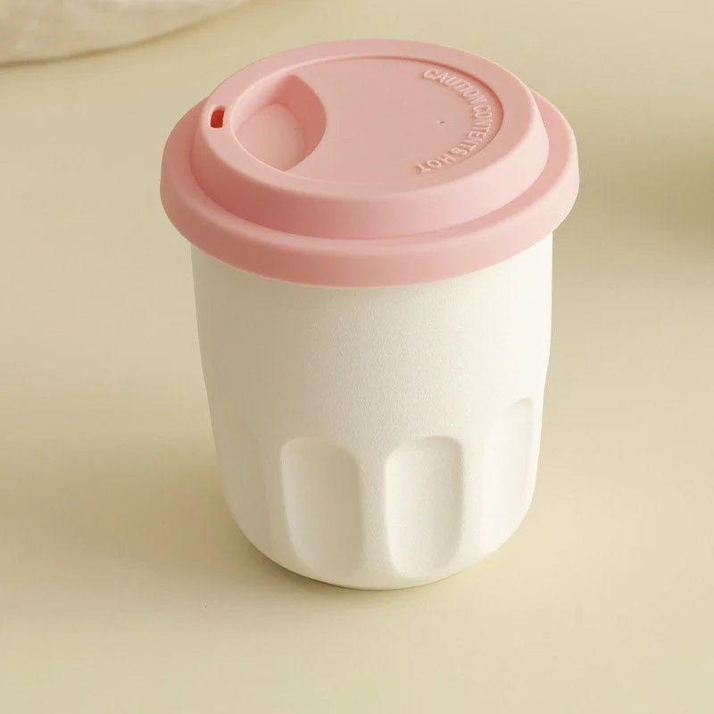 Front view of the cream white frosted ceramic reusable coffee cup with its pink silicone lid on. - RoomDen