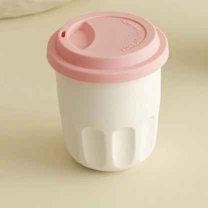 Front view of the cream white frosted ceramic reusable coffee cup with its pink silicone lid on. - RoomDen