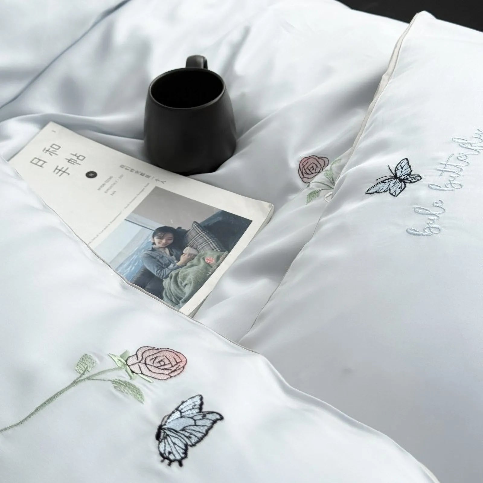 Top-down view of the Cloud Blue bedding with a book and mug, showcasing the fine embroidery details on the duvet and pillowcase.