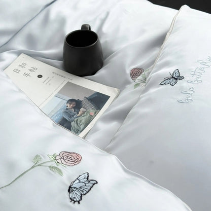 Top-down view of the Cloud Blue bedding with a book and mug, showcasing the fine embroidery details on the duvet and pillowcase.