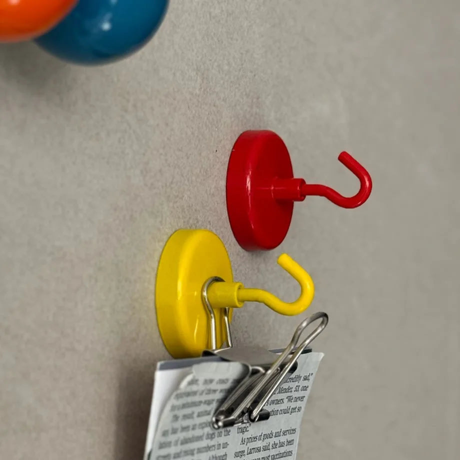 Red and yellow magnetic hooks on a grey wall, with the yellow hook holding a metal binder clip - RoomDen