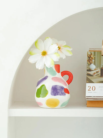 The single-handle spotty ceramic vase holding white flowers, styled in a white arched shelf nook next to a calendar. - RoomDen