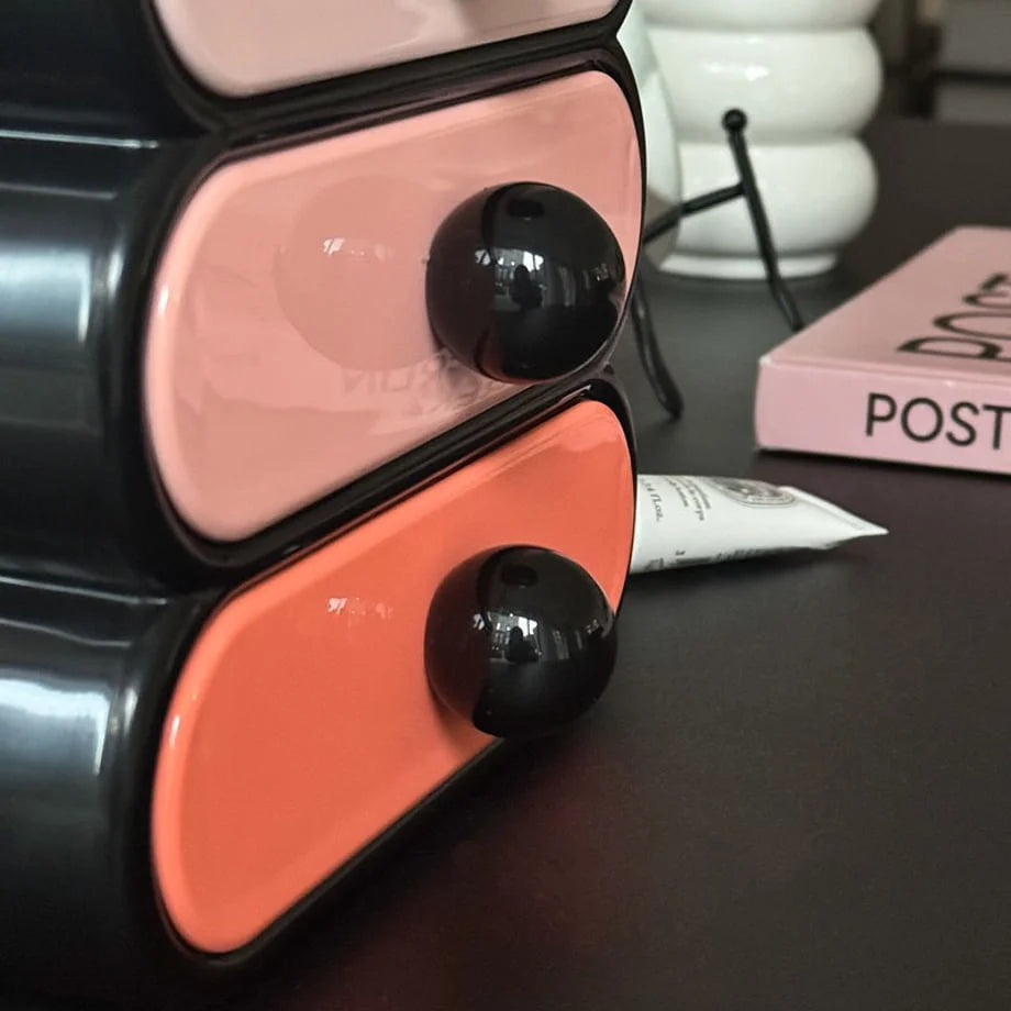 Macro shot of the round black knobs on the pink and orange drawers of the makeup organizer.