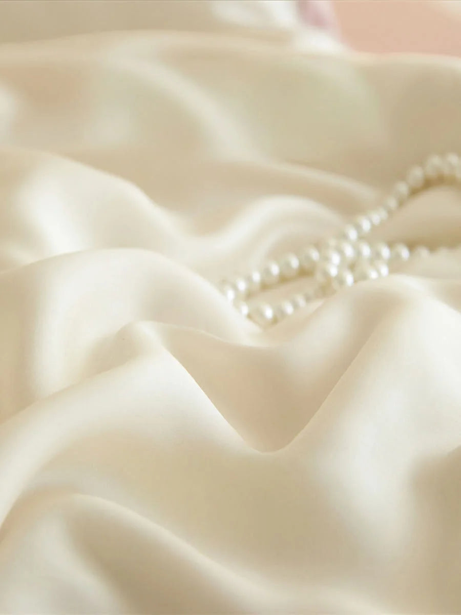 Extreme close-up of the silky smooth cream-colored Cooling Tencel fabric with a pearl necklace. - RoomDen