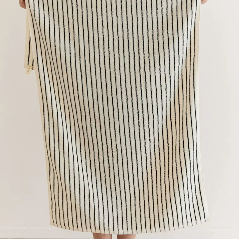 Full view of the white and black striped cotton bath towel held up to show its length and pattern.
