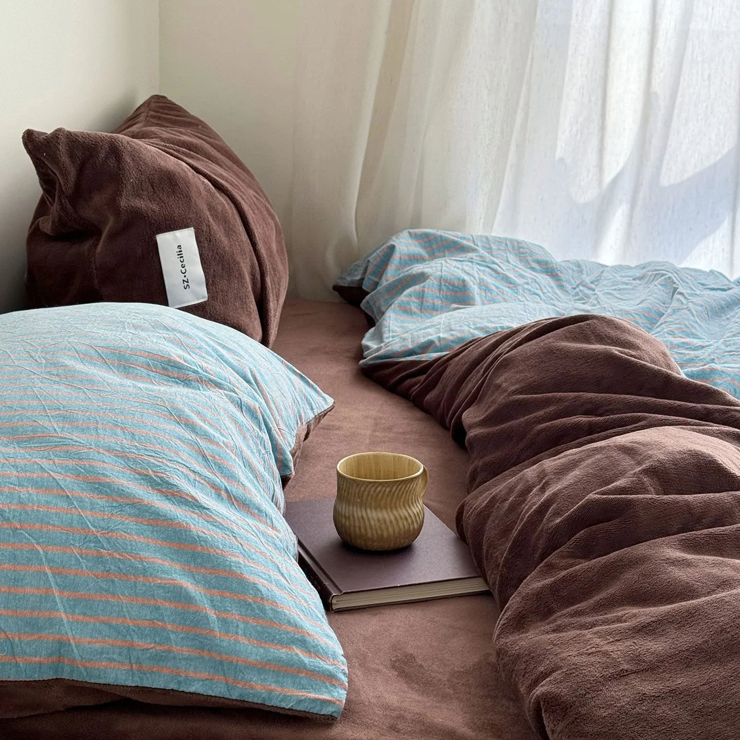 The Brown & Blue reversible bedding set styled with books and a mug near a window.