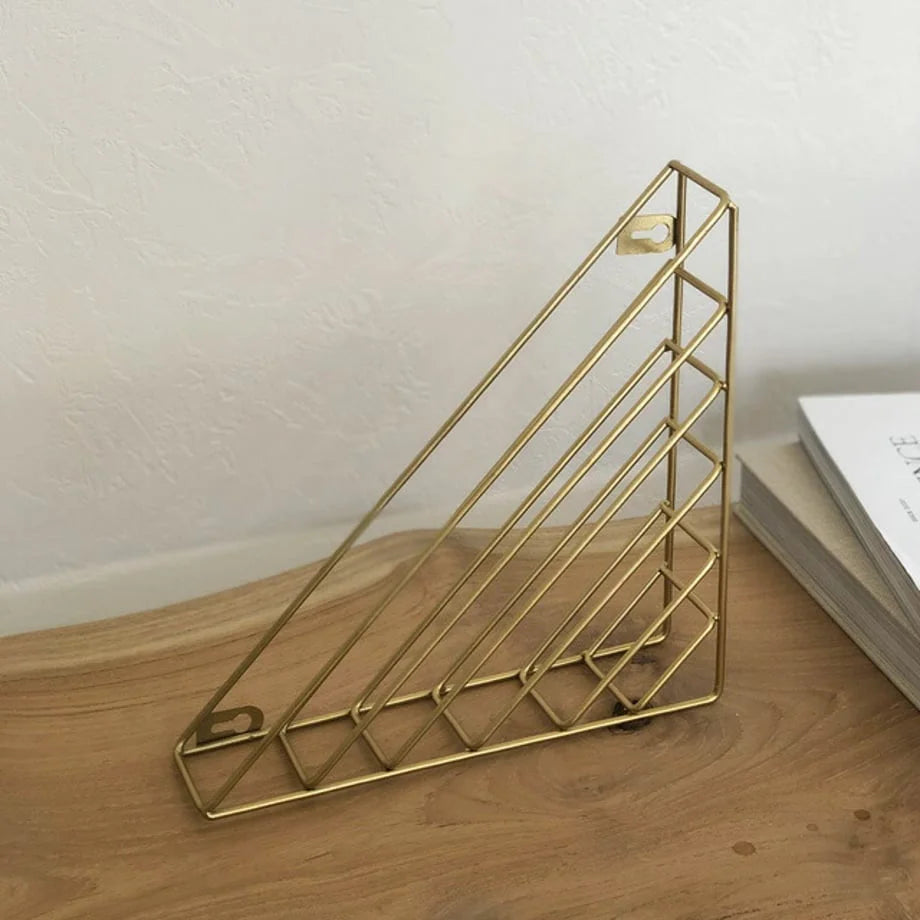 Empty Gold Wireframe Magazine Rack standing on a light wood surface, showing mounting holes - RoomDen