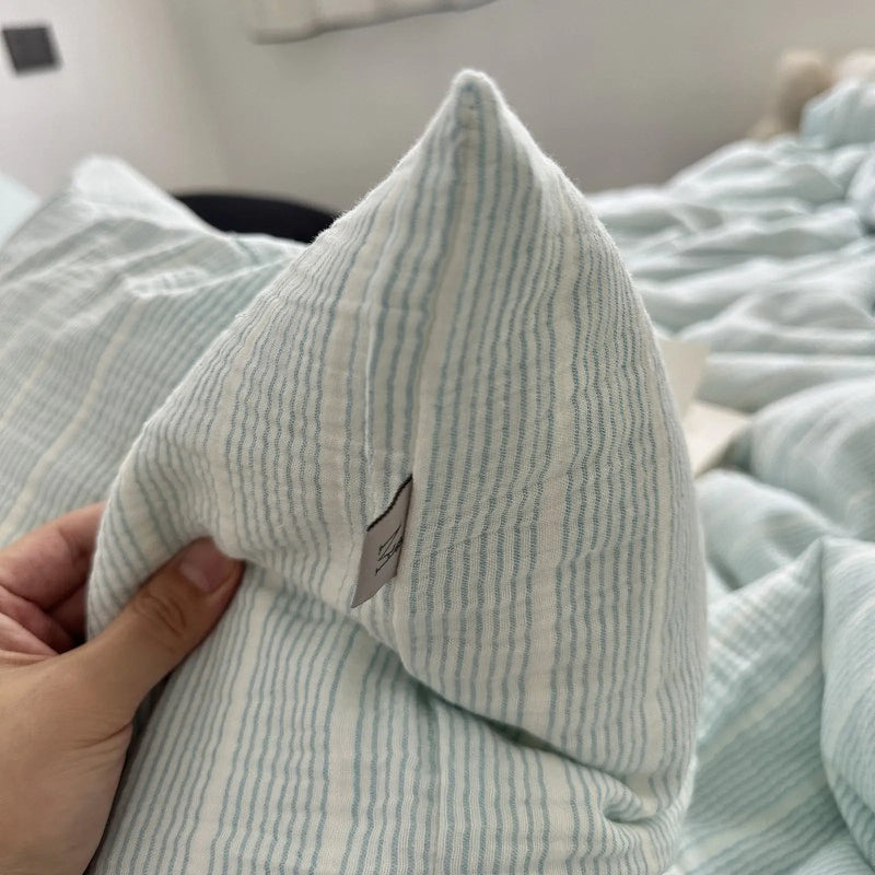 Hand holding the corner of a cyan pinstripe washed cotton pillowcase, showing how softly the fabric folds.