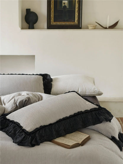 Close-up of the pinstripe pillows with black ruffle trim, with a book resting on them and art on a shelf behind. - RoomDen