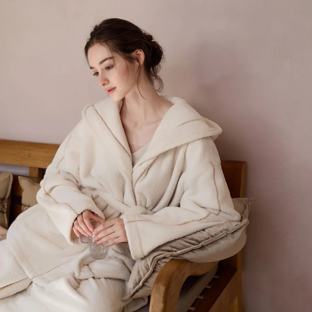 Model sitting comfortably on a bench in a cozy, creamy white flannel fleece pajama set, looking down at a glass - RoomDen.