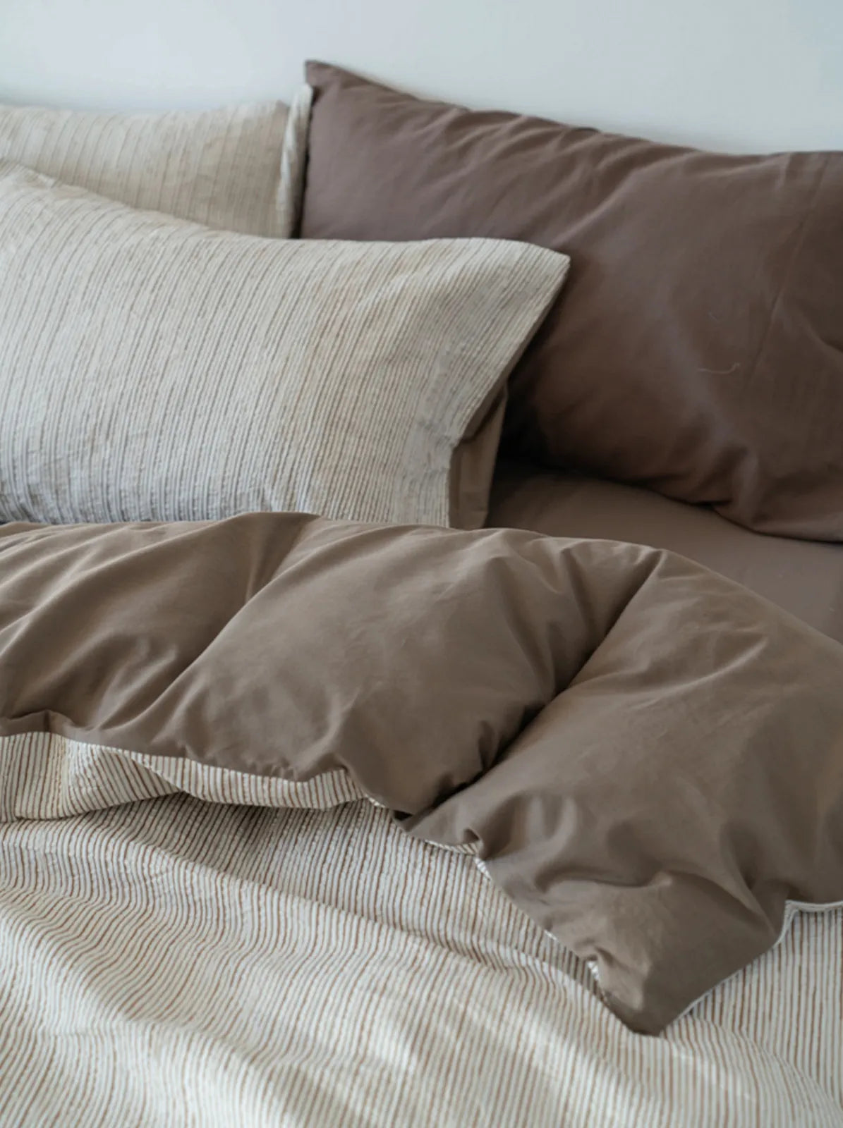 Close-up view highlighting the contrast between the pinstripe pillowcase and the solid brown pillowcase.
