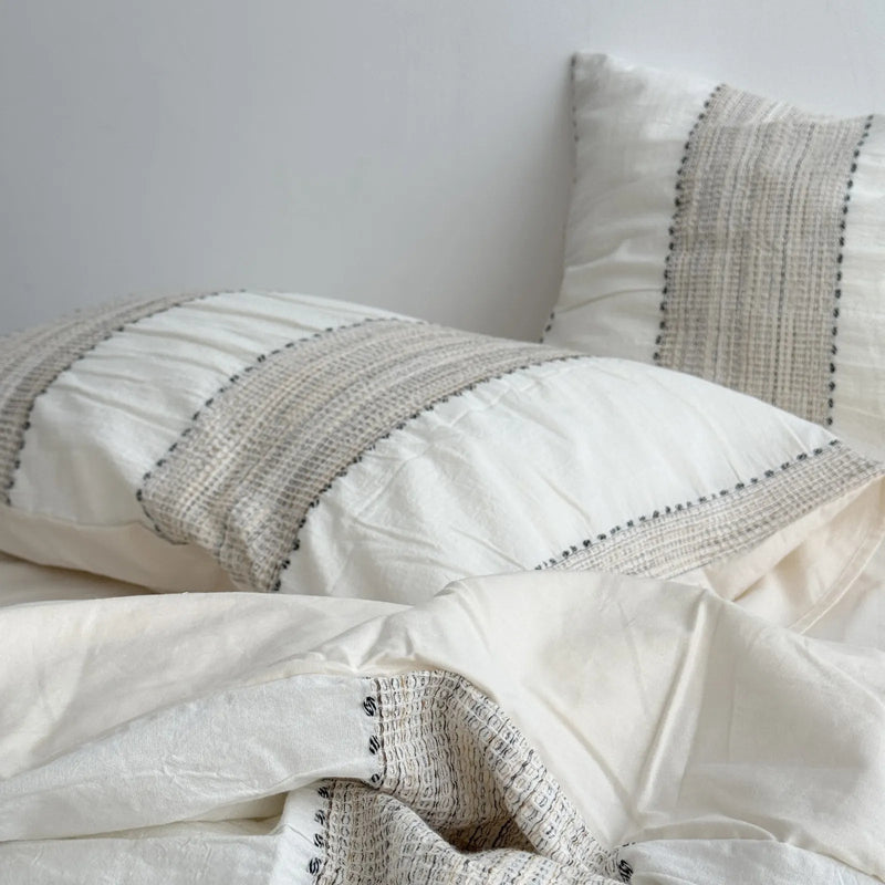 Close-up of the textured woven stripe on an oatmeal beige pillowcase, layer one of the Soft-Stack Method. - RoomDen