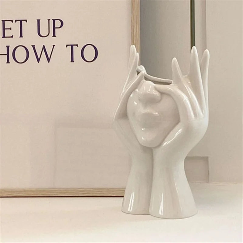 White resin 'Peekaboo' face vase shown against a neutral art print - RoomDen.