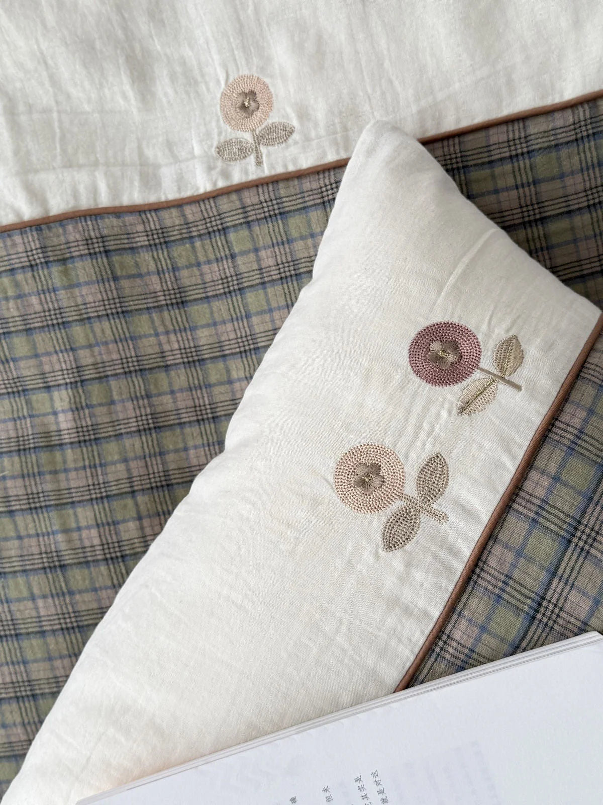 Detailed shot of the delicate floral embroidery on the beige section of the pillowcase, next to the plaid pattern. - RoomDen
