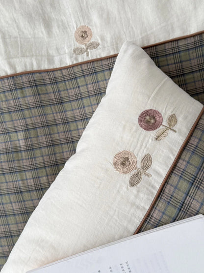 Detailed shot of the delicate floral embroidery on the beige section of the pillowcase, next to the plaid pattern. - RoomDen