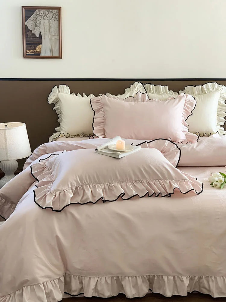 Lifestyle shot of the Blush Pink ruffled bedding set, styled with a candle and a framed picture in the background - RoomDen.